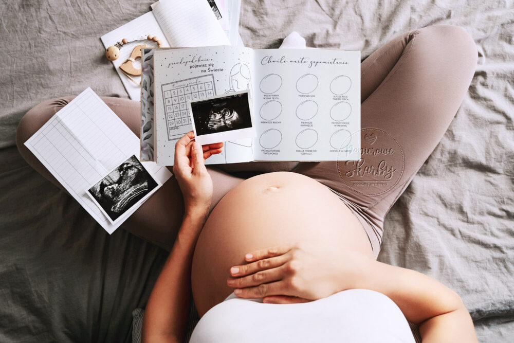 kobieta w ciąży ze zdjęciem usg notująca w albumie ciążowym od brzuszka do maluszka papierowe skarby